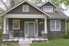 a gray house with white trim on the front door and porch, sitting next to a green lawn