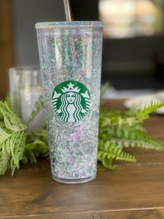 a starbucks cup with glitter and a straw in it on a table next to ferns