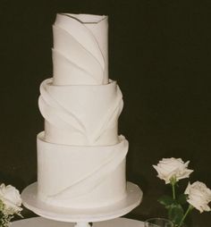 a three tiered white cake sitting on top of a table next to some flowers