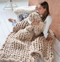 a woman is laying on the floor wrapped in a giant chunky blanket and looking at the camera