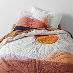 a bed with two pillows on top of it and an orange blanket over the head