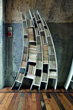 a bookshelf with many books on it next to a white surfboard in front of a concrete wall