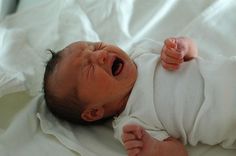 a baby is yawning while laying on its back in a white sheeted bed