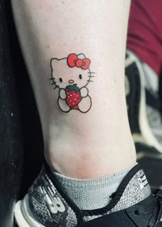 a hello kitty tattoo on the ankle with a strawberry in it's left foot