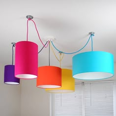 four different colored lamps hanging from the ceiling in a room with white walls and windows