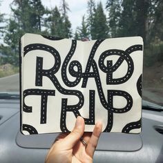 someone holding up a book with the words road trip written on it