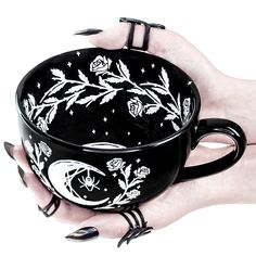 a woman's hand holding a black coffee cup with white flowers and moon designs on it