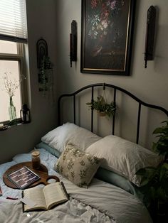 an open book on a bed with pillows and plants in the window sill next to it