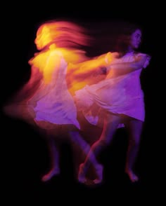 two women in white dresses are dancing with colored lights on their backs and arms,