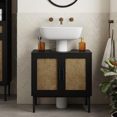 a white sink sitting under a mirror next to a black cabinet with baskets on it