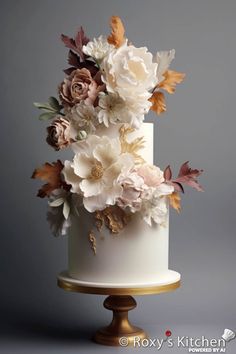 a white wedding cake with flowers on the top and gold trimmings is displayed against a gray background