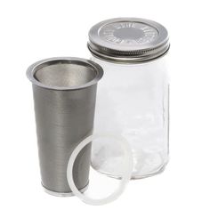 a glass jar with a metal lid and an empty cup next to it on a white background