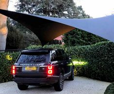 an suv is parked in front of some bushes and trees with a large triangular shade over it