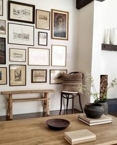 a wooden table topped with a vase filled with flowers next to a wall covered in pictures