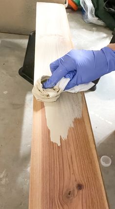 a person in blue gloves waxing a piece of wood with white paint on it