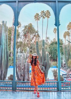 a woman in an orange dress and straw hat is standing by a cactus covered area