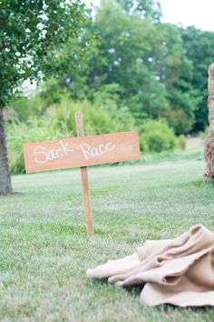 a wooden sign sitting on top of a lush green field next to a pile of hay