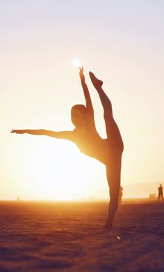 a woman is doing yoga on the beach in front of the sun with her arms stretched out