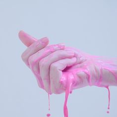 a hand with pink paint on it holding something in the air and dripping from its fingers