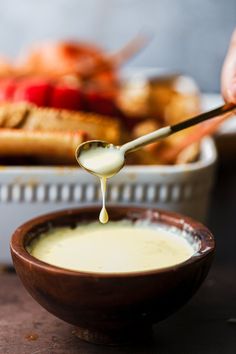 a spoon is being drizzled with cream over a bowl full of food