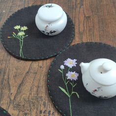 two teapots with flowers painted on them are sitting on black coasters next to each other