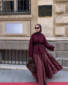 a woman in a long dress and hijab walking down the street