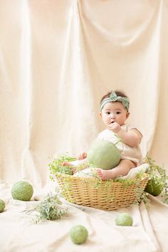 a baby sitting in a basket with green balls around it