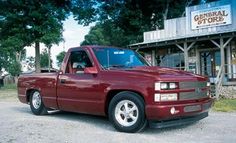 a red pickup truck parked in front of a general store on the side of a road