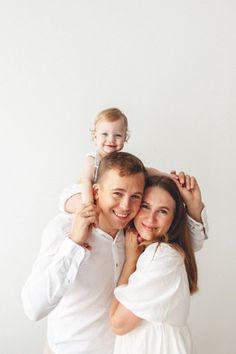 a man, woman and child are posing for a family photo in front of a white wall