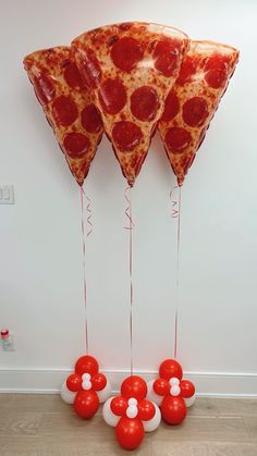 three slices of pizza on sticks with balloons attached to them in front of a white wall