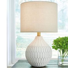 a white table lamp sitting on top of a wooden table next to a vase filled with green plants