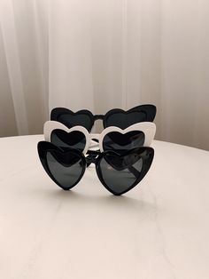 black and white heart shaped sunglasses sitting on top of a table with curtains in the background