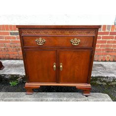 an old wooden cabinet with brass handles on the front and side doors, sitting in front of a brick wall