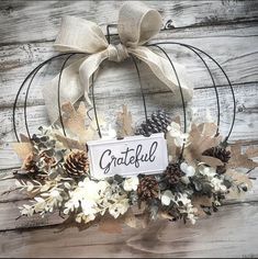 a wreath with pine cones and white flowers is hanging on a wooden wall next to a sign that says grateful