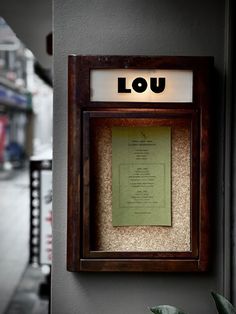 a wooden frame with a sign that reads lou on it and a plant next to it