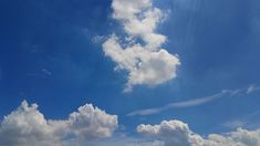 two people on the beach flying kites under a blue sky with white fluffy clouds