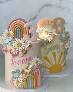 two cakes decorated with flowers and rainbows on top of each other, one has the number three