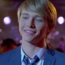 a young man with blonde hair wearing a blue suit and tie smiling at the camera