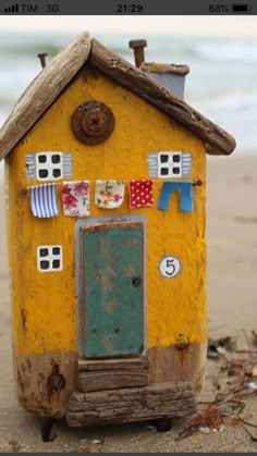 a small yellow house sitting on top of a sandy beach next to the ocean with clothes hanging from it's roof