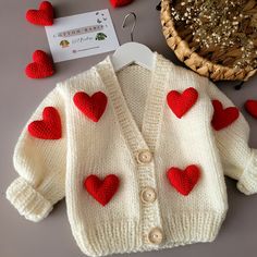 a knitted sweater with red hearts on it next to a basket and cardigan