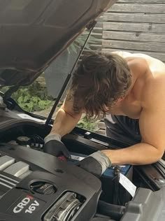 a shirtless man working on an engine in the hood of a car with plants growing out of it