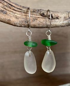 two white and green sea glass earrings hanging from a tree branch with silver earwires