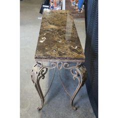 a marble top console table with metal legs and scroll work on the base, in a store