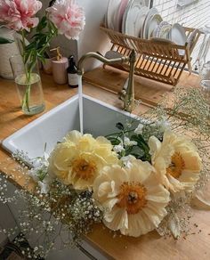 some flowers are sitting in the sink on top of a wooden counter with dishes and utensils