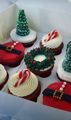 twelve decorated christmas cupcakes in a box with candy canes on the top