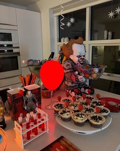 a table topped with cupcakes covered in icing and a creepy clown face