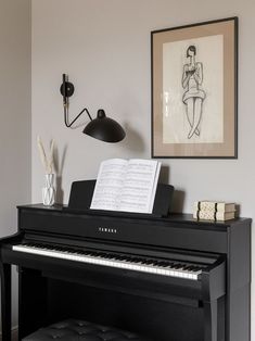 a black piano sitting in front of a painting on the wall next to a lamp