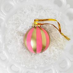 a pink and gold striped ornament sitting on top of white shredded paper in a bowl