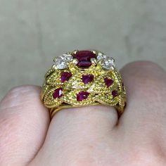 a close up of a person's hand holding a ring with red and white stones