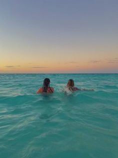 two women are swimming in the ocean at sunset